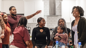 A big family of many generations laughing and singing together in a kitchen.
