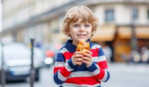 Happy child on street eating a croissant.