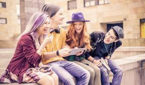 A group of multiracial teenagers laughing while reading on a computer tablet.
