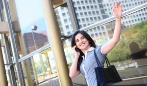 A business woman waving goodbye at office building.