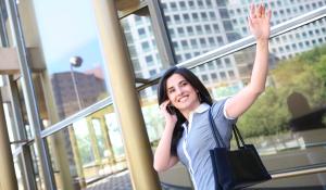 A business woman waving goodbye at an office building.