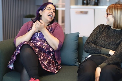 Two women talking and sitting together on a couch. 