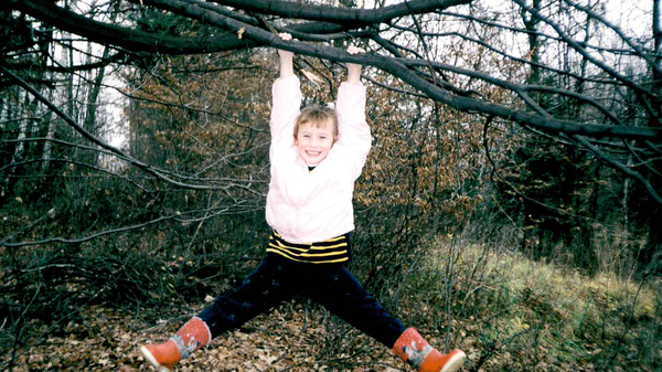 Young girl hanging from a tree and grinning at the camera.