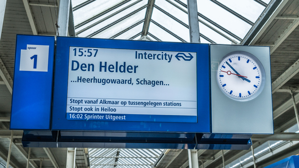 A blue and white display showing information about a train departure in Dutch, with an analog clock next to it.