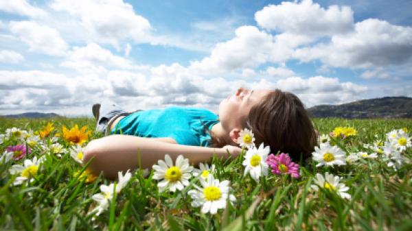 Woman laying in grass looking up at blue sky.