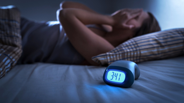 A woman lying awake at night, with an alarm clock showing 3:41.