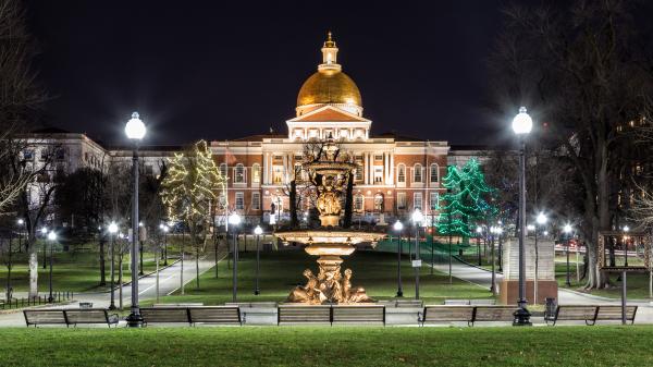 A lit up Massachusetts State House seen from Boston Common at night.