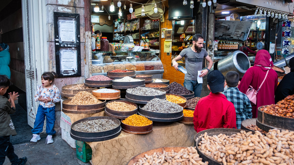 A bearded shop owner filling a bag in front of a shop selling nuts, with people watching him.