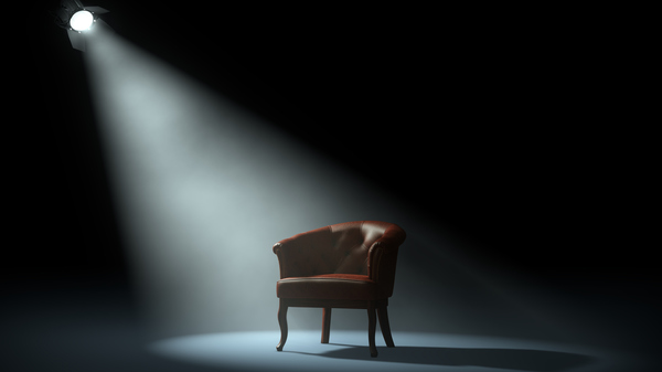 Empty red leather armchair standing in a dark space with a spotlight shining on it.