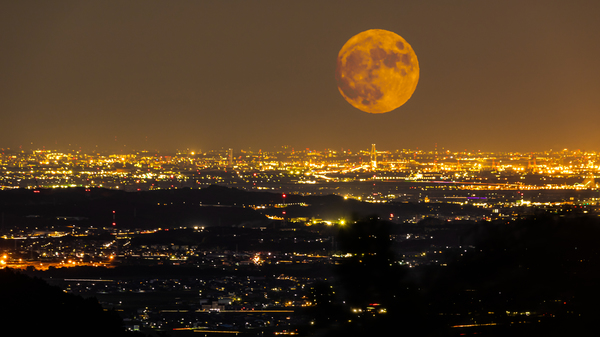 A big orange Full Harvest Moon over the city lights of Yokkaichi city in Mie prefecture, Japan.