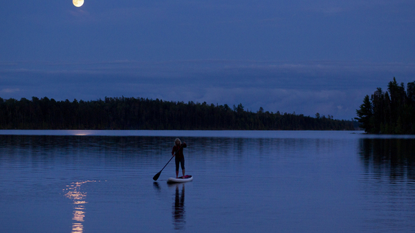 A woman goes for a stand up paddleboard trip at night under a full moon on a small lake in Ontario, Canada.