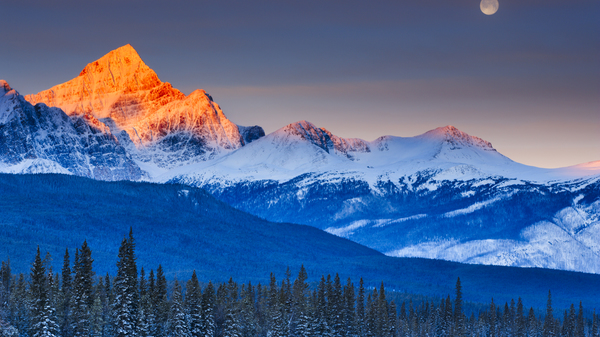 The Full Moon setting over Mount Edith Cavell and other snowy mountains in Jasper National Park, Canada.
