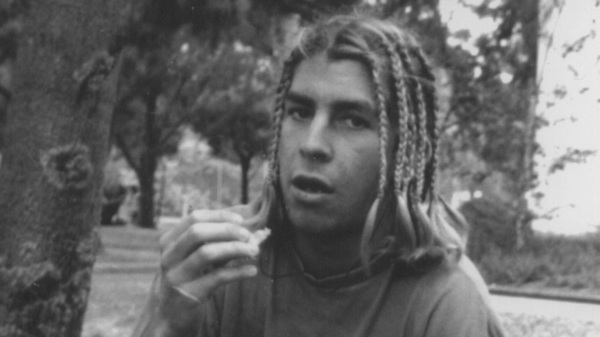 A young man with braids looking at the camera and eating chips.