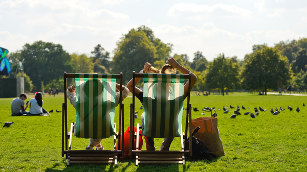 Two people sitting in deck chairs in a sunny park.