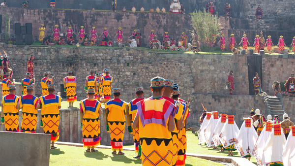 Men and women lined up in front of an Incan temple with yellow, pink and white colorful dress.