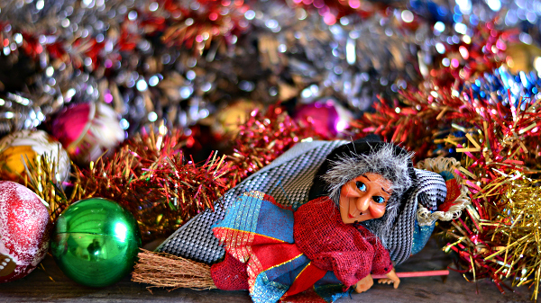 Figure of a witch riding a broom in front of Christmas decoration.