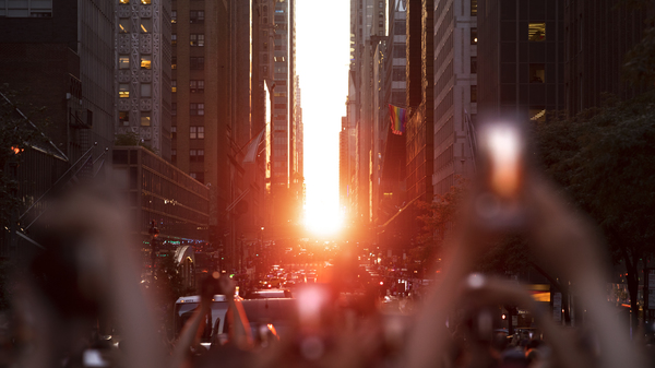 People taking pictures with their phones of the Sun setting between the skyscrapers on Manhattan, New York, US.