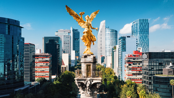 Aerial view of Independence Monument Mexico City. The monument is a golden angel glimmering in the Sun with the skyscrapers of the city behind it.