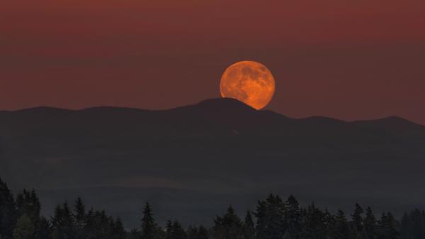 Full Moon rising over Oregon mountain range landscape at dusk.