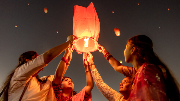 Four women releasing a lit yellow sky lantern into a dark sky filled with more yellow lanterns.