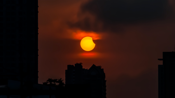 A partial eclipse of the Sun seen next to buildings.
