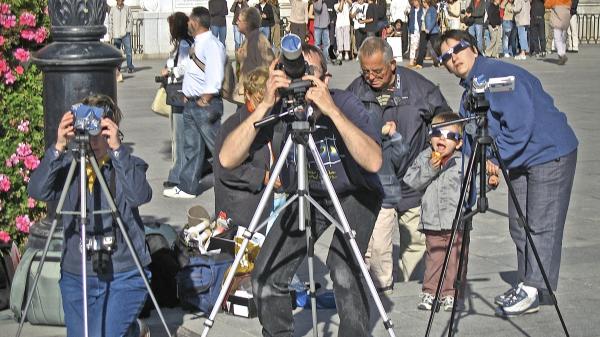 People watching a solar eclipse through cameras and eclipse glasses.