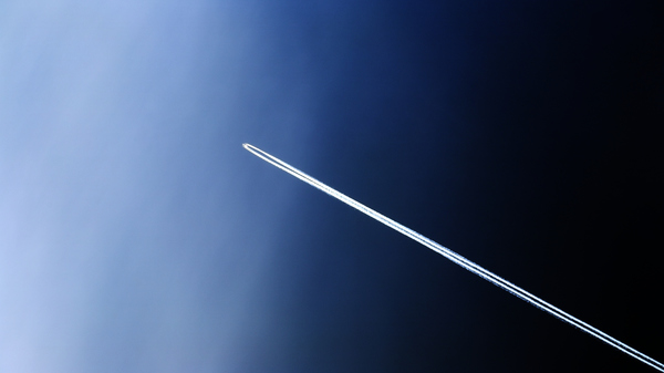 View of a plane high in the daytime sky, with two contrails trailing behind.