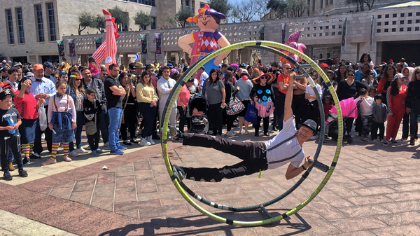 A street performer doing acrobatics for a large crowd on a street in Israel during Purim celebrations.