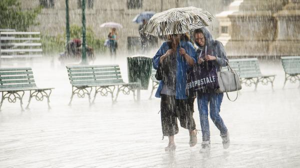 Two women walking under umbrella during heavy rain.