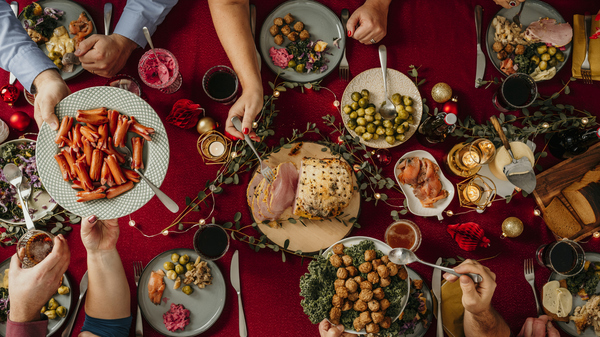 A festive Scandinavian Christmas dinner table with plates of meatballs, ham, vegetables, and traditional dishes being shared.