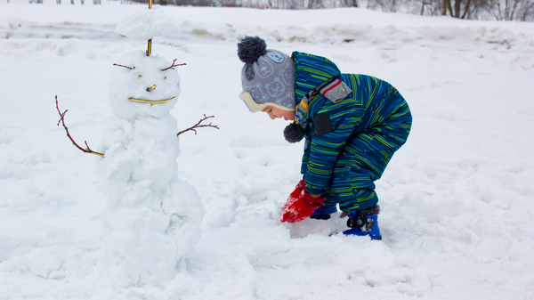 A four-year-old child, a boy, smiling rolls a snowball and sculpts a snowman