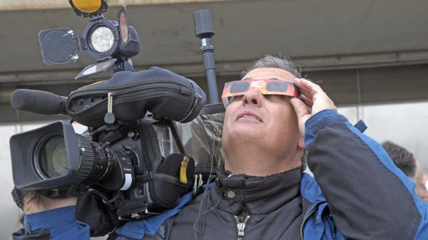 A man with a camera and wearing solar eclipse glasses watching a solar eclipse.