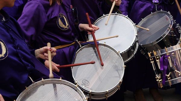 Drummers dressed in typical purple easter clothes and playing ornamented drums in a procession.