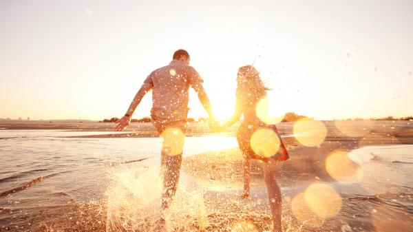 A happy couple running through the waves on a sunlit beach.