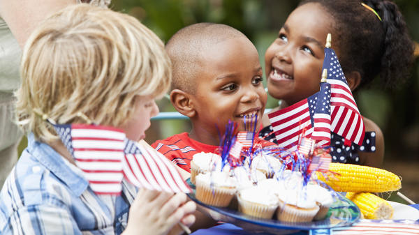 Three kids at an American barbecue eating cupcakes