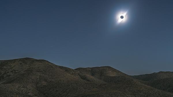 Dark skies over hills and an eclipsed Sun in the sky.