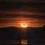 Between layers of clouds, a partial solar eclipse is seen at sunrise over Rice Lake, Ontario, as the sun, partially covered by the moon, rises in a beautiful orange sky above the trees and water.