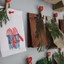 Close-up of a handmade advent calendar with small bags, greenery, and numbered heart-shaped clips on a wall.
