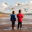 2 kids watching seagulls at low tide on a beach