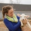 Female farmer holding a lamb licking its mouth. 