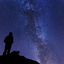 A person standing on a rocky outcrop looking up at the Milky Way in a dark and starry sky.