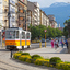 A yellow tramway is winding its way through the aging cityblocks of Sofia, Bulgaria. The street shows blue mountains in the horizon.