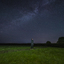 A person standing in lit up green grass looking up at a dark and starry sky.