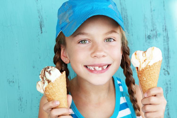 Portrait of 7 year old kid girl eating two ice creams.