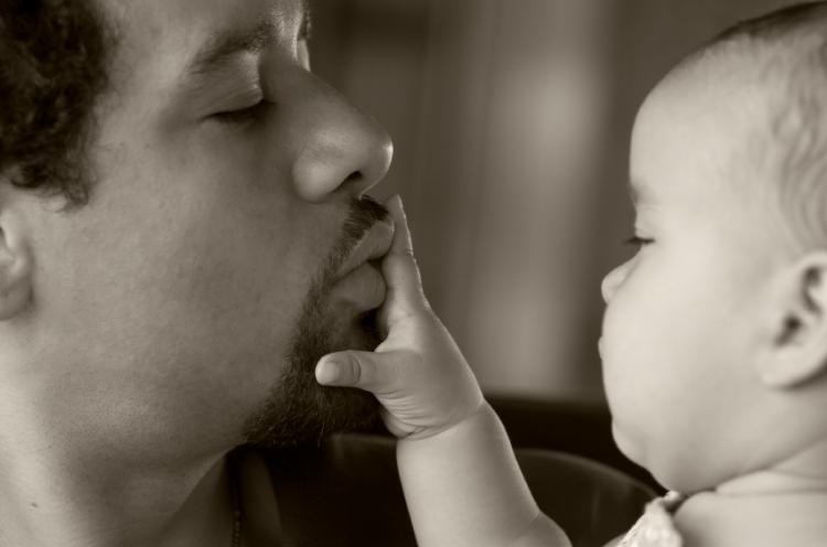 A father lovingly playing with his baby. Black and white image slightly sepia toned.