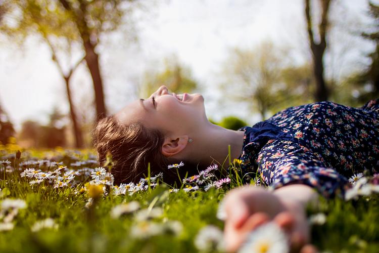 Молодая девушка, лежащая в траве под весенним солнцем в окружении ромашек.