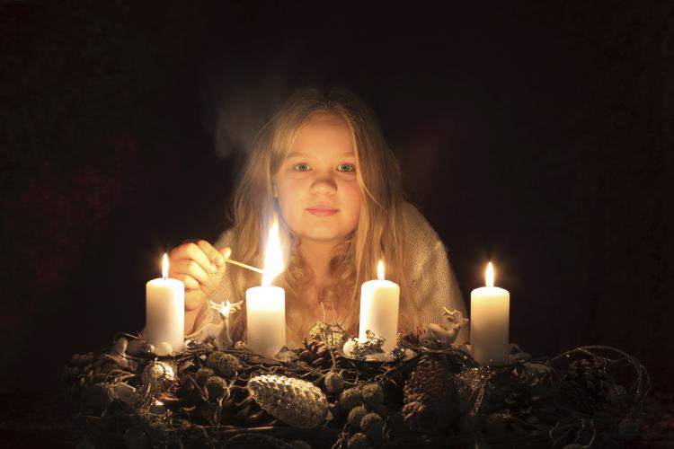 En ung jente tenner det fjerde lyset på en adventsstake.