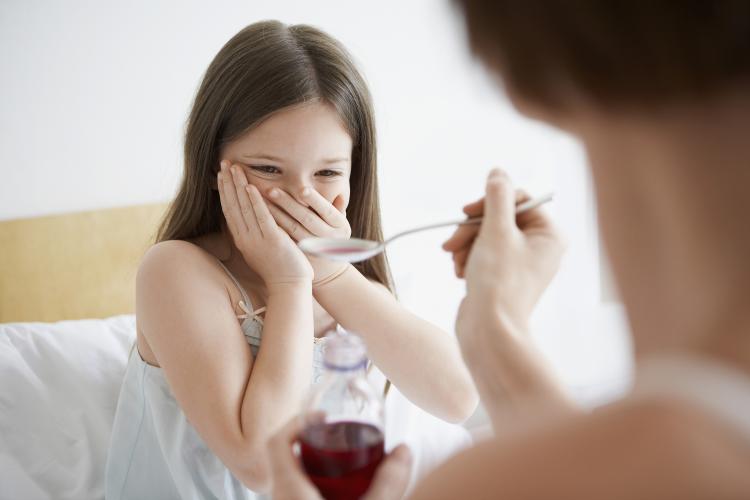 Mother trying to give medicine to sceptical daughter.