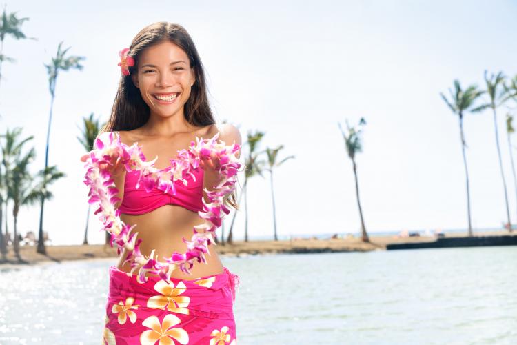 A young woman dressed in Aloha wear holding up a Hawaiian pink lei.