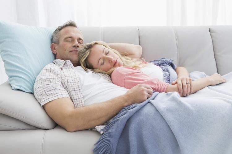 Couple napping under a blanket on the couch.